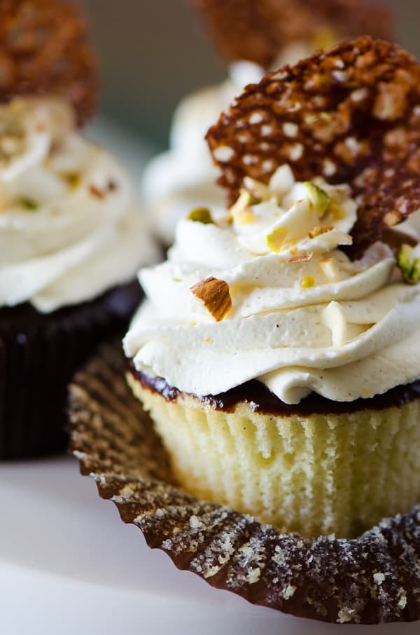 Cannoli Cupcakes with Chocolate Pistachio Crunch | Holy cannoli, what a cupcake! These vanilla-almond Cannoli Cupcakes are stuffed and topped with a classic sweet ricotta filling, glazed with a layer of chocolate ganache, and garnished with some pretty fancy food art.