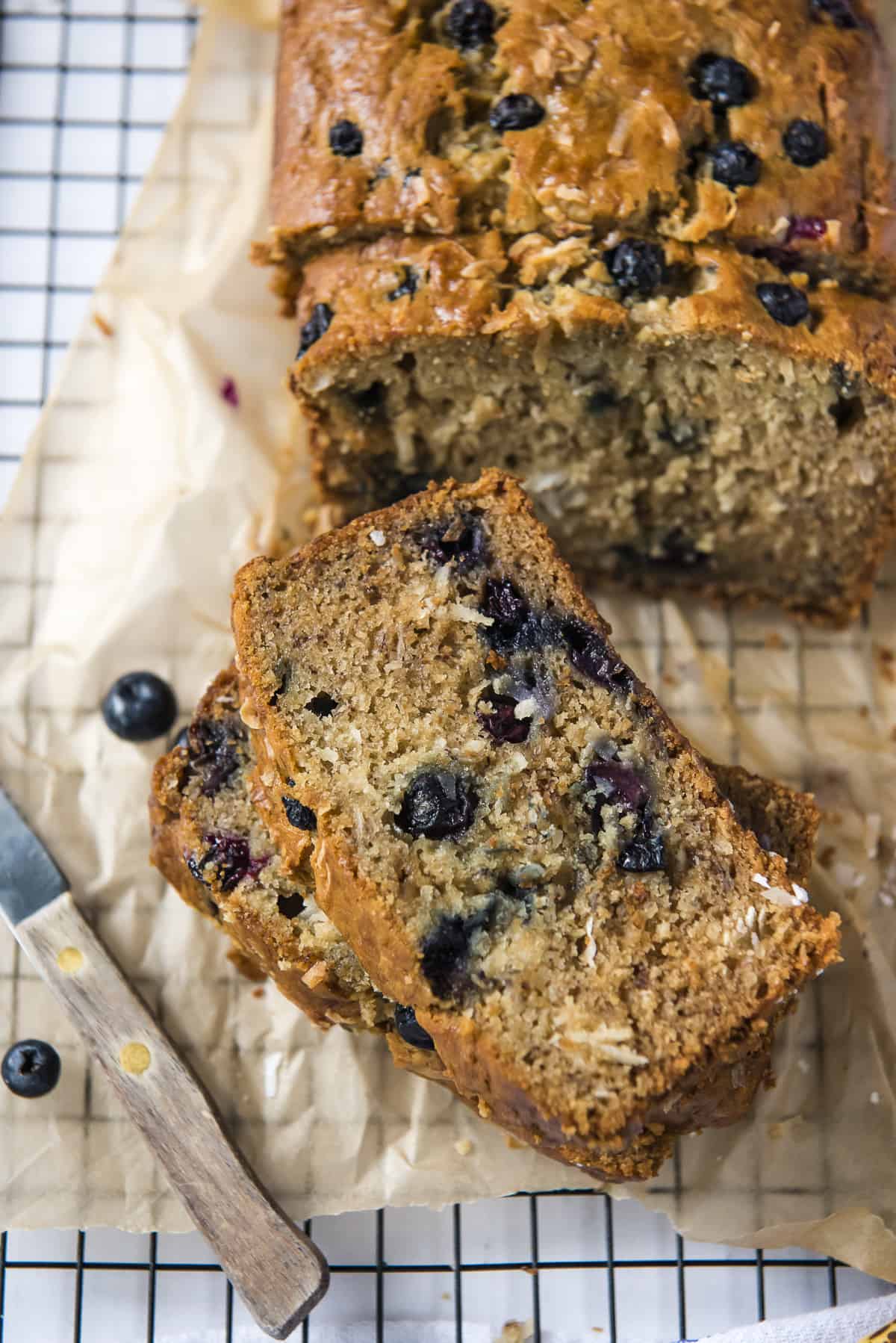 slices of blueberry coconut banana bread on a cooling rack with a knife