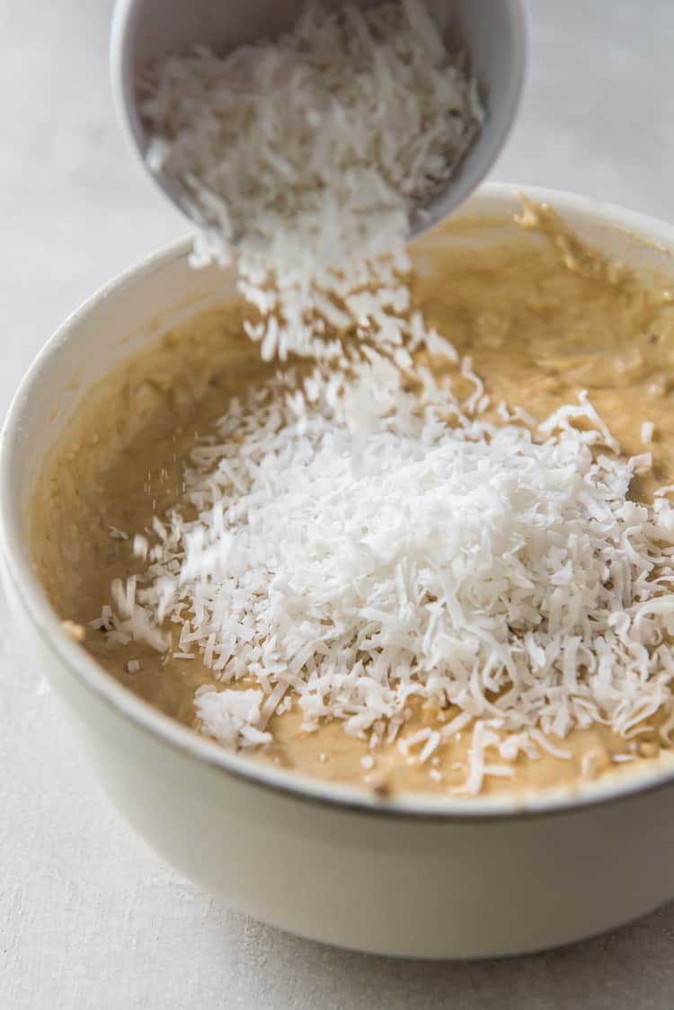 a bowl of shredded coconut being added to a bowl of batter