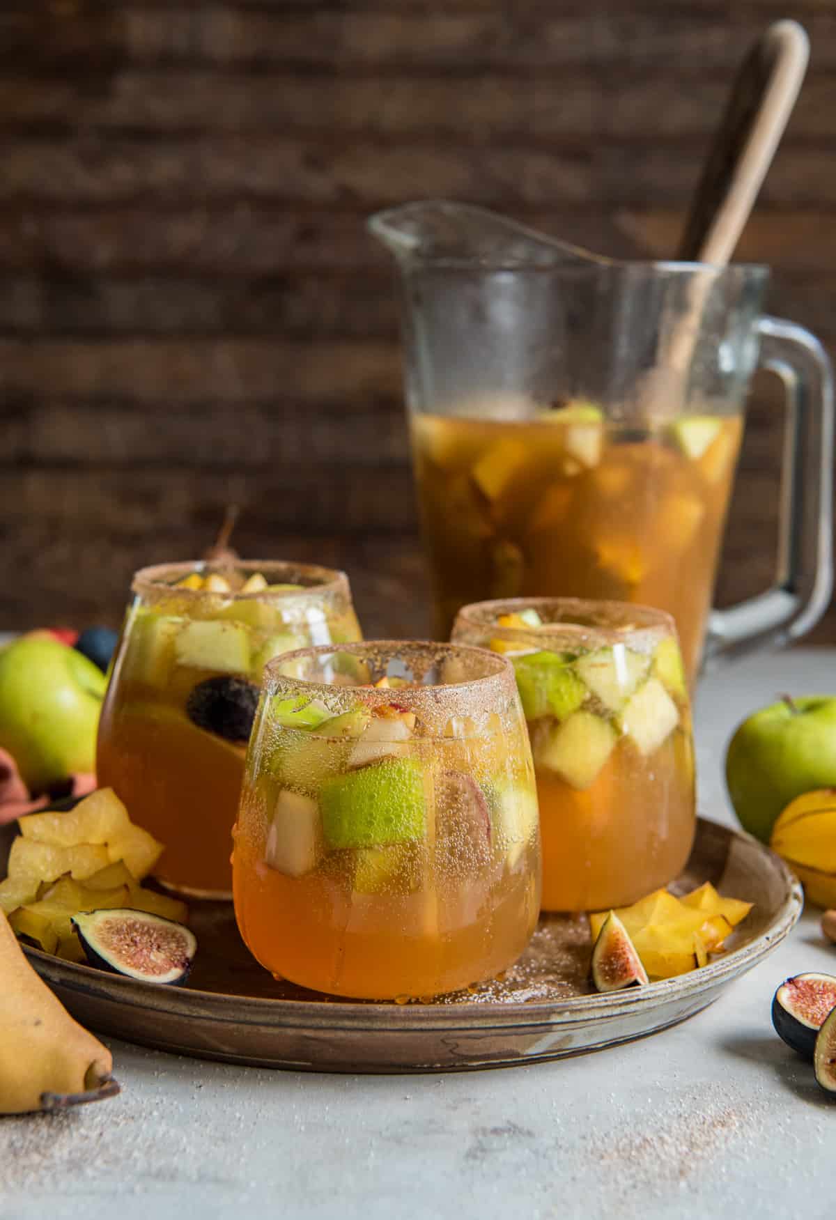 Three glasses of fall sangria with fruit and a pitcher.
