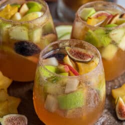 Three glasses of fall sangria with fruit on top.