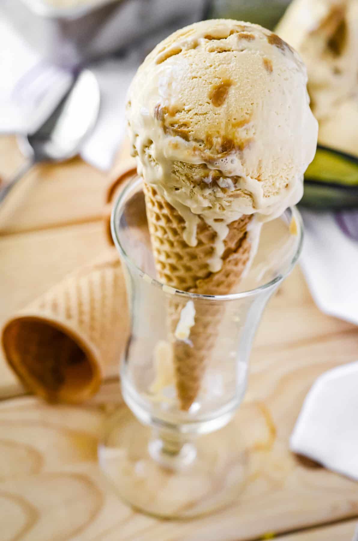 a scoop of dripping dulce de leche ice cream in a sugar cone, set in a tall glass