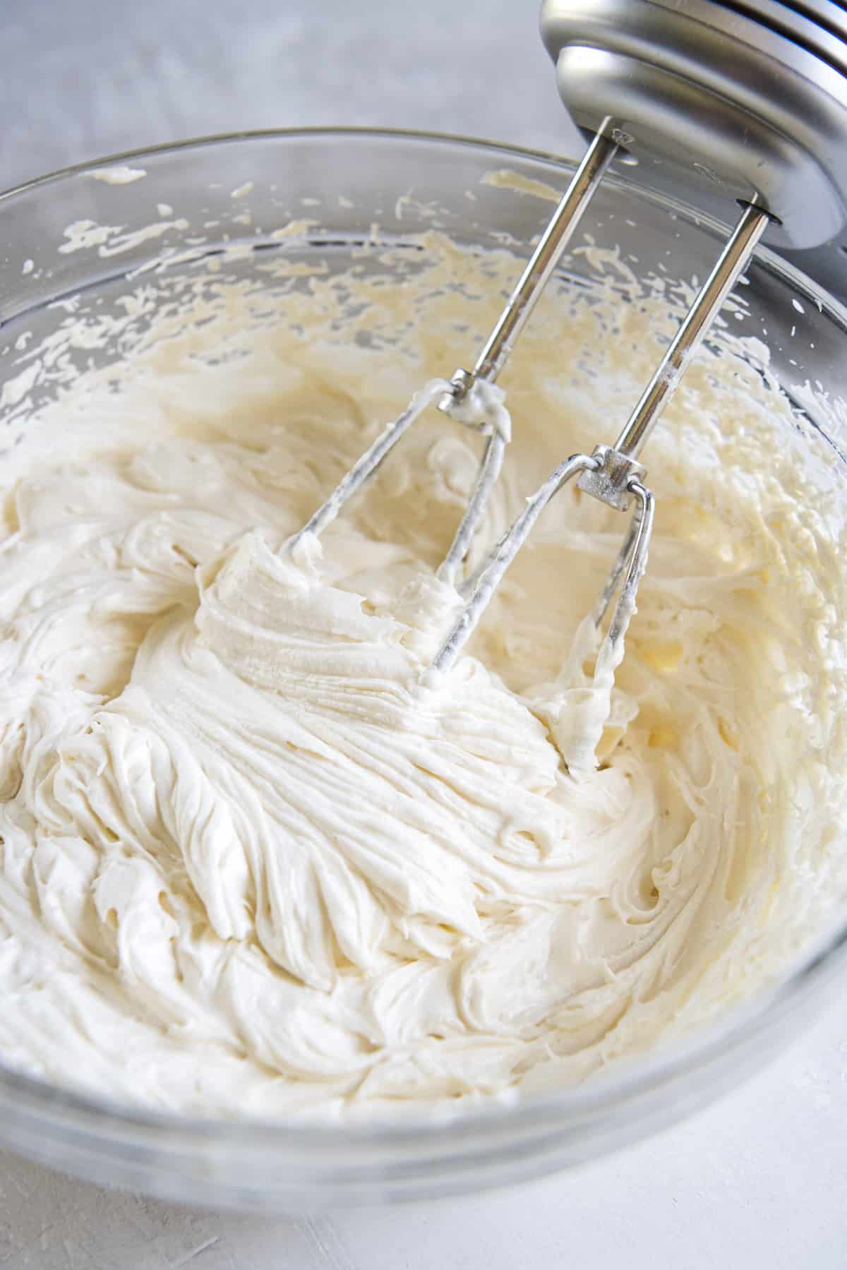 a bowl of whipped cream cheese frosting with a hand mixer set next to it