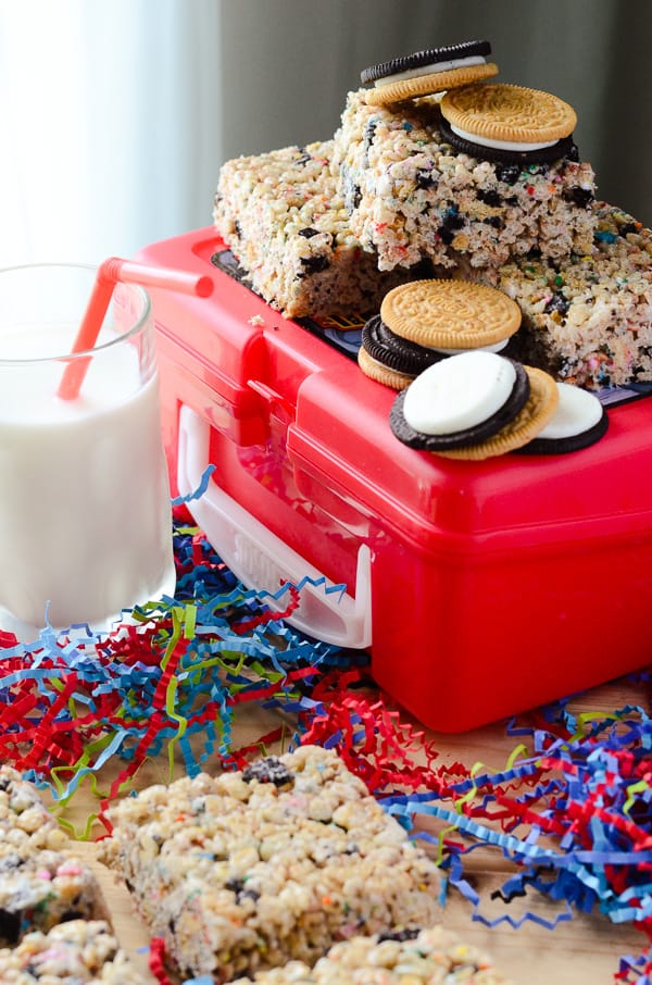 Squares of Oreo Rice Krispie Treats, confetti, milk and a red lunch box