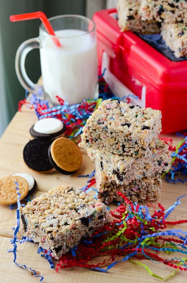 Stacked Squares of Oreo Rice Krispie Treats, confetti, milk and a red lunch box