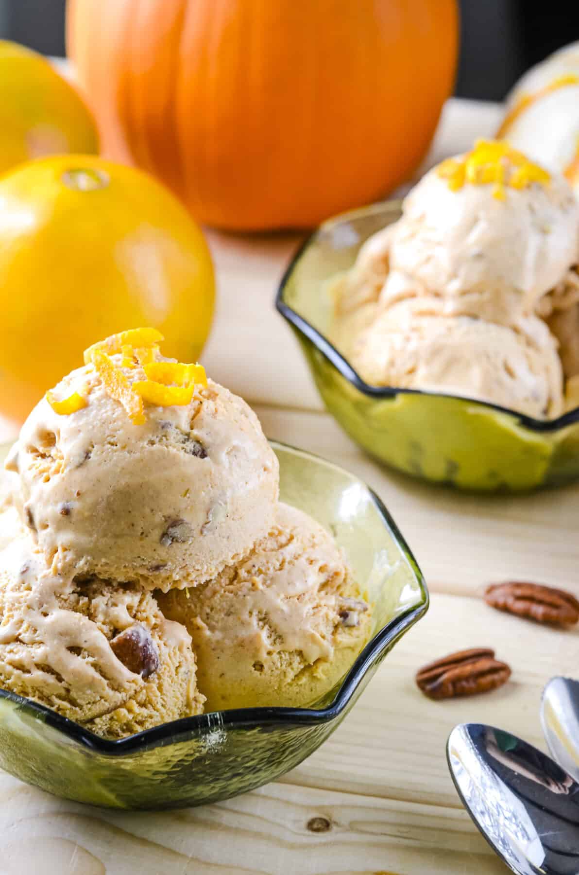 two bowls of pumpkin ice cream surrounded by pecans, orange wedges, and spoons