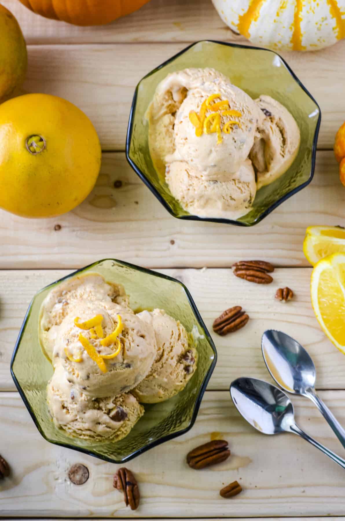 an above shot of bowls of pumpkin ice cream surrounded by pecans, orange wedges, and spoons
