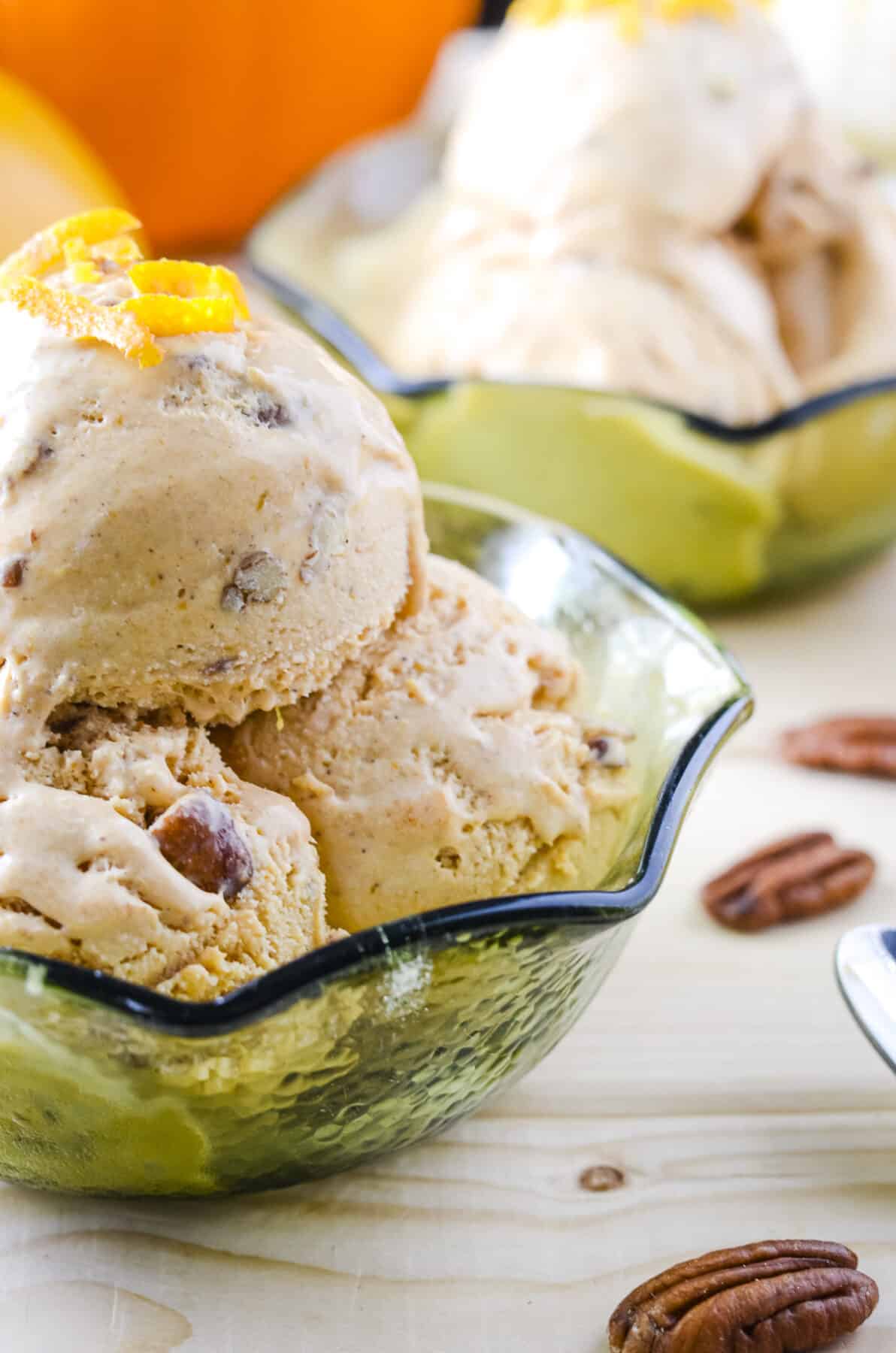 scoops of pumpkin ice cream in a green glass bowl surrounded by pecans