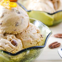 scoops of pumpkin ice cream in a green glass bowl surrounded by pecans