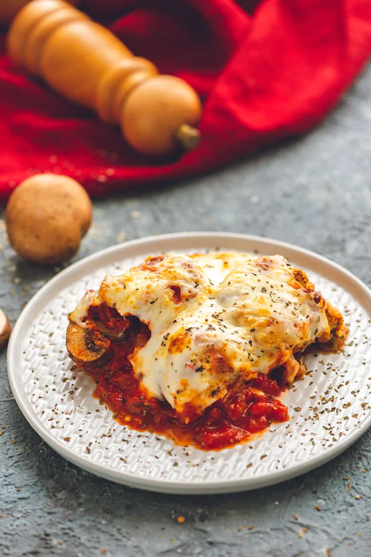 A slice of Baked Eggplant Parmesan on a plate with mushrooms scattered around
