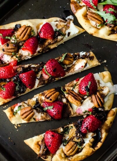 A chicken flatbread pizza with strawberries and pecans on a baking sheet.