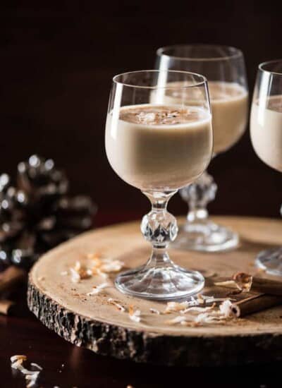 Three glasses with a Coquito on a wooden board.