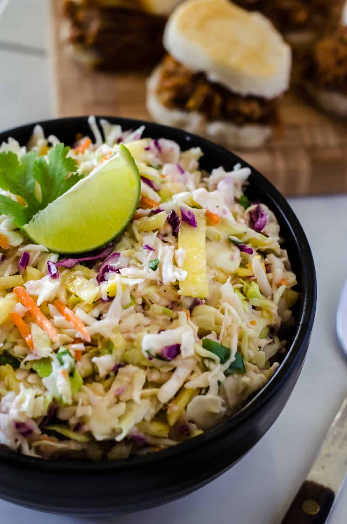pineapple coleslaw in a black bowl with a fresh lime wedge on top
