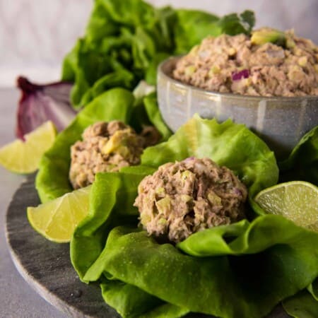 A bowl of tuna and avocado salad served in fresh lettuce wraps with lime wedges on a slate plate.