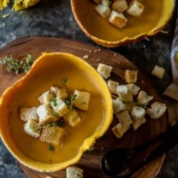 Two bowls of pumpkin beer cheese soup with croutons on a wooden board.