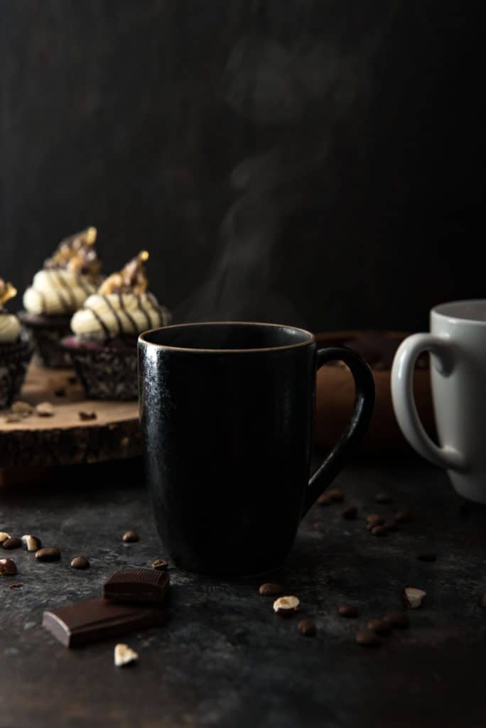 steaming coffee mugs with mocha cupcakes in the background