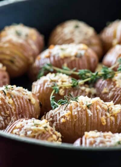 Hasselback Potato Bites roasted in a skillet with sprigs of thyme.