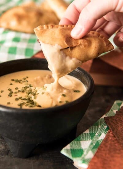 dipping Smoked Sausage and Peppers Empanadas in cheese dip