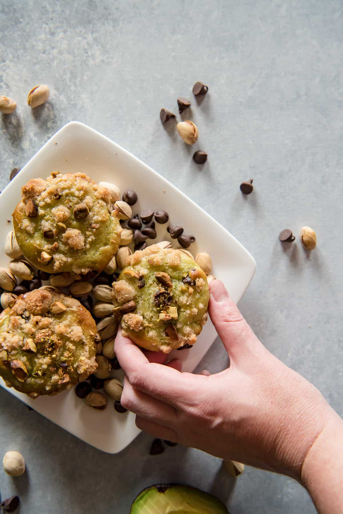 A hand lifting an avocado muffin from a plate.