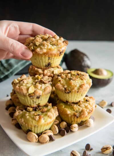 A hand holding a stack of avocado muffins with chocolate chips scattered on top.
