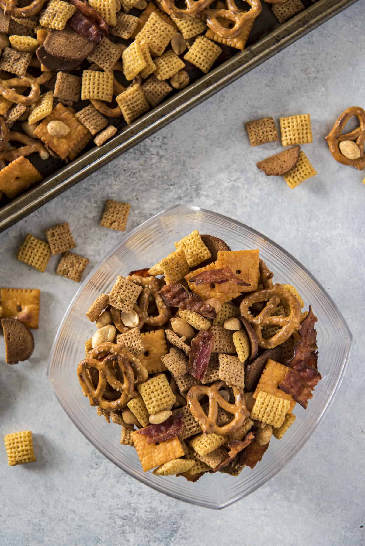 top shot of a bowl of bacon chex mix next to a sheet pan with chex mix on it