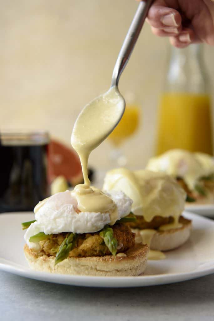 Pouring hollandaise sauce on top of a Crab Cake Benedict