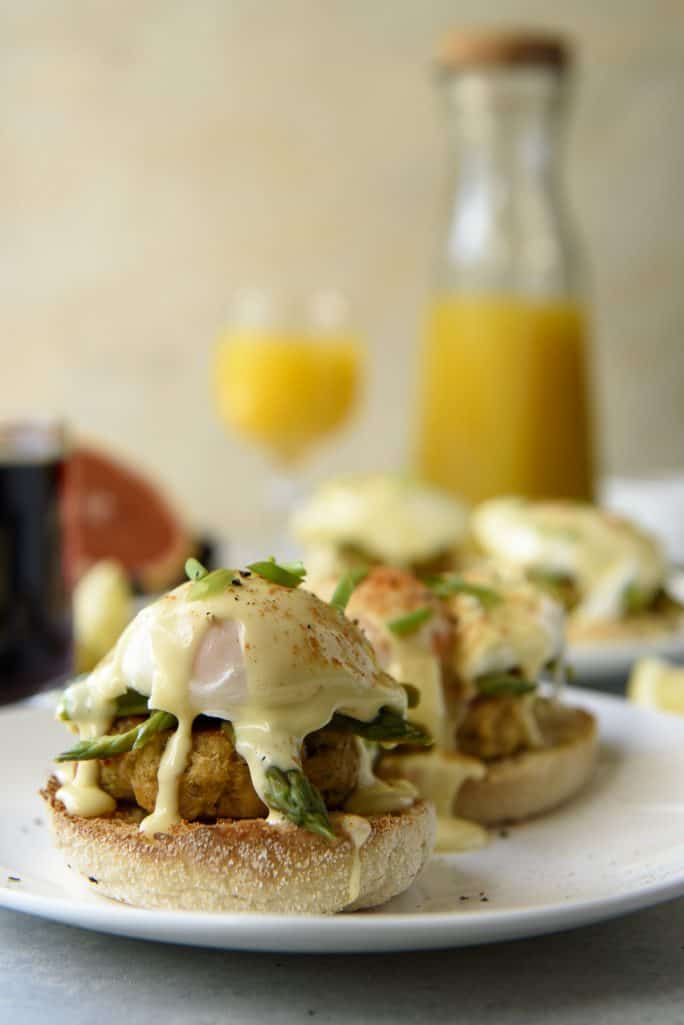 Asparagus and Crab Cake Benedict on a white plate with orange juice in the background