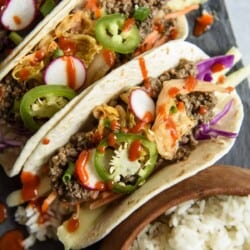 Three beef bulgogi tacos on a plate with rice and vegetables.
