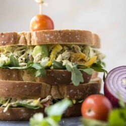 An avocado chicken salad sandwich is stacked on top of a plate.