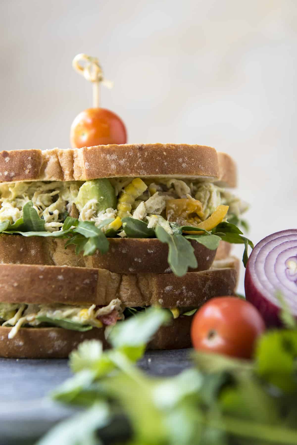 An avocado chicken salad sandwich is stacked on top of a plate.