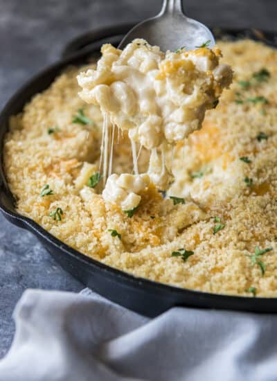 baked mac and cheese in a cast iron skillet with a scoop being lifted out