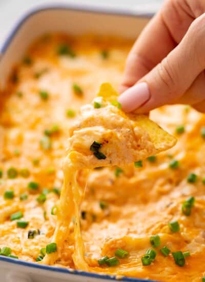 A hand dipping a tortilla chip in a dish of Buffalo Chicken Dip