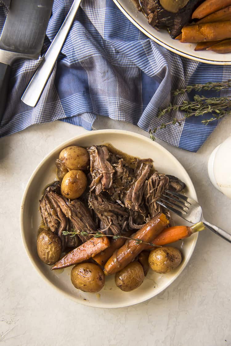 a top view of chuck pot roast, potatoes, and carrots on a white plate with a fork