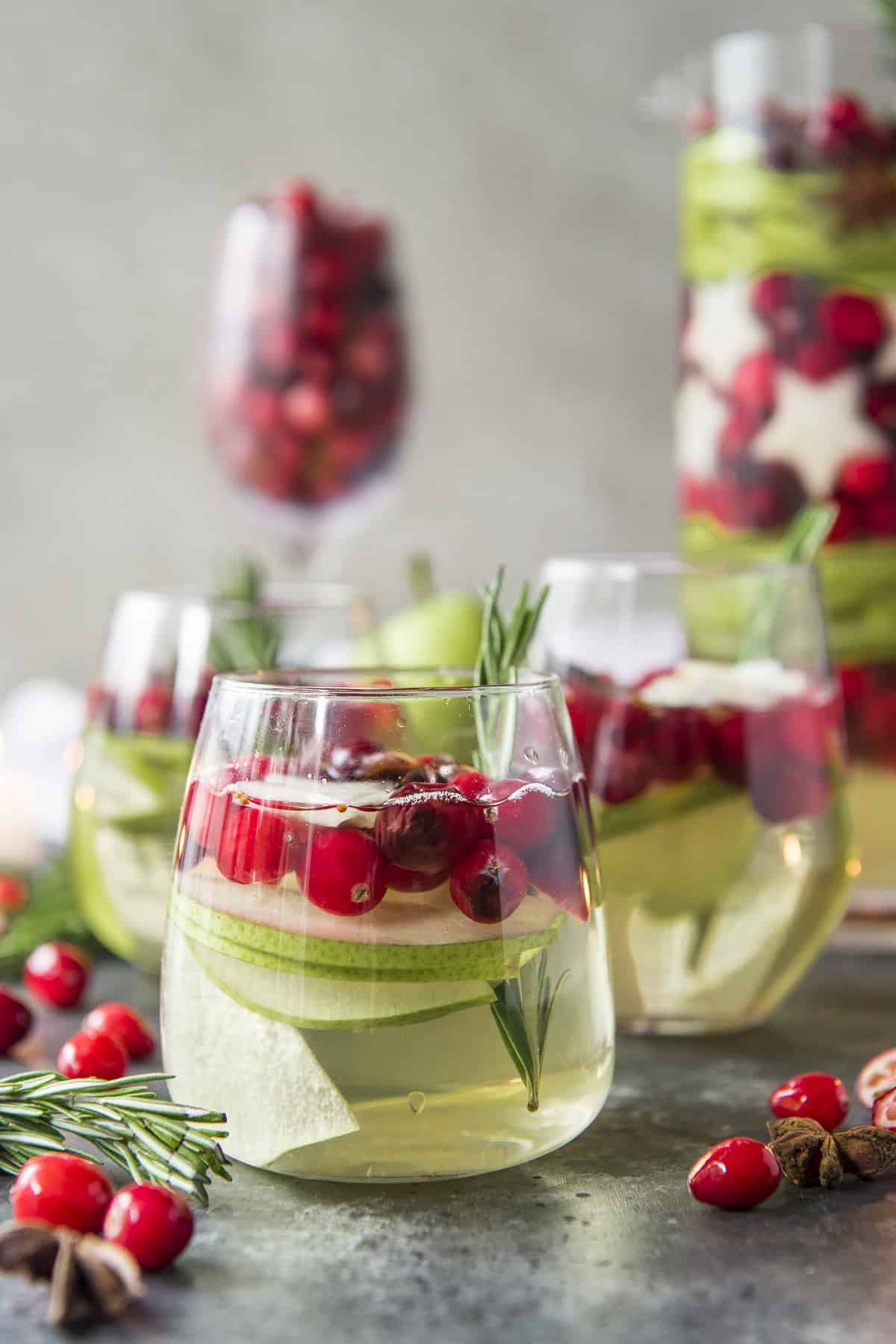 3 glasses of white Christmas sangria with scattered cranberries on a gray surface