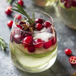 Close up of a glass of white wine Christmas sangria full of pears, cranberries, anise, and rosemary.