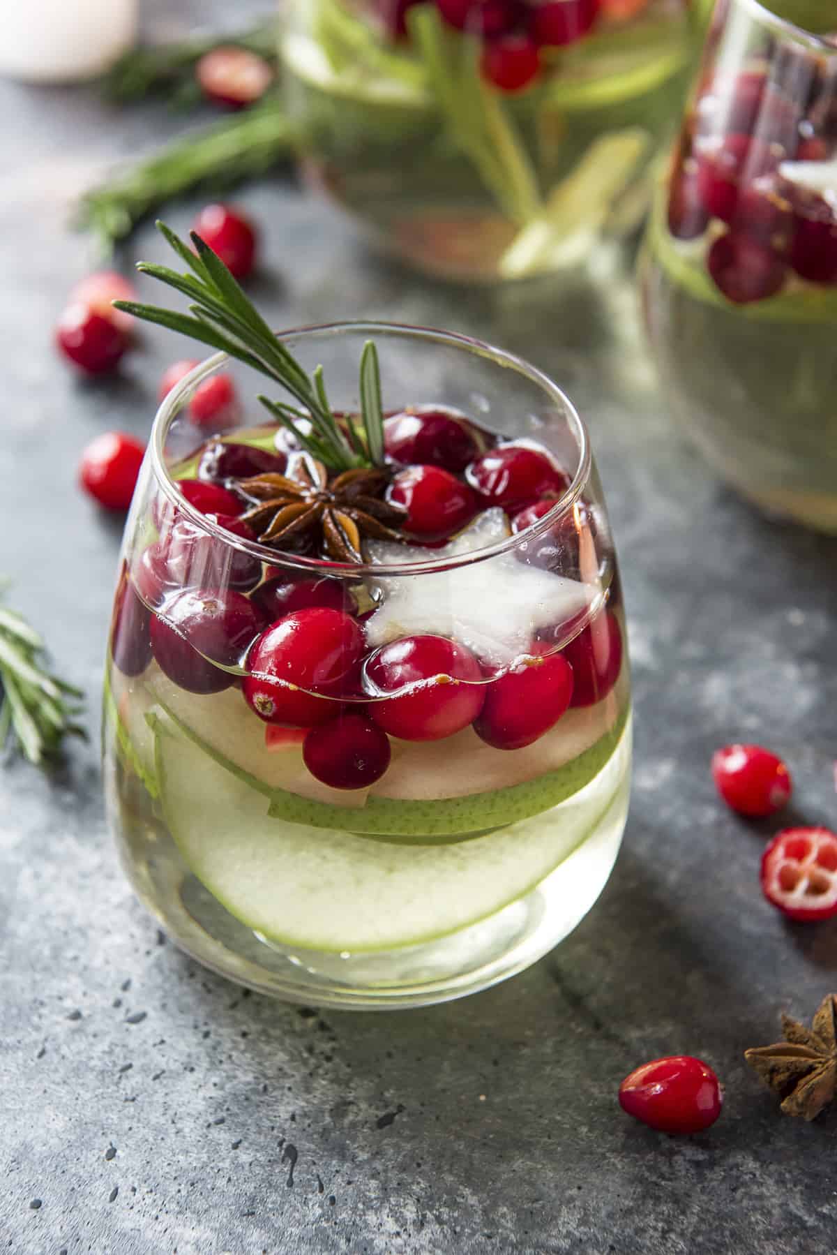 Close up of a glass of white wine Christmas sangria full of pears, cranberries, anise, and rosemary