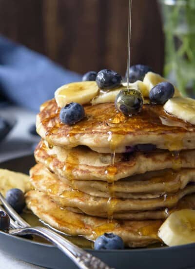 A closeup of syrup being drizzled on a stack of Blueberry Banana Pancakes
