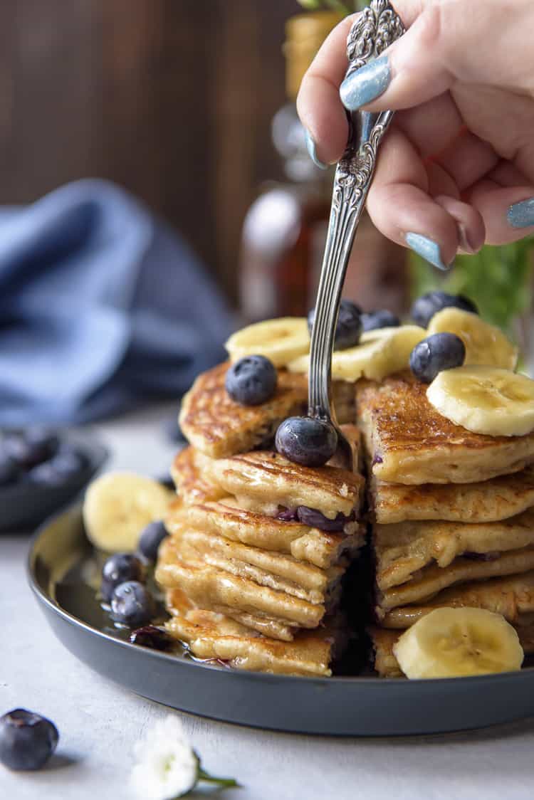A fork cutting into a plate of buttermilk Blueberry Banana Pancakes