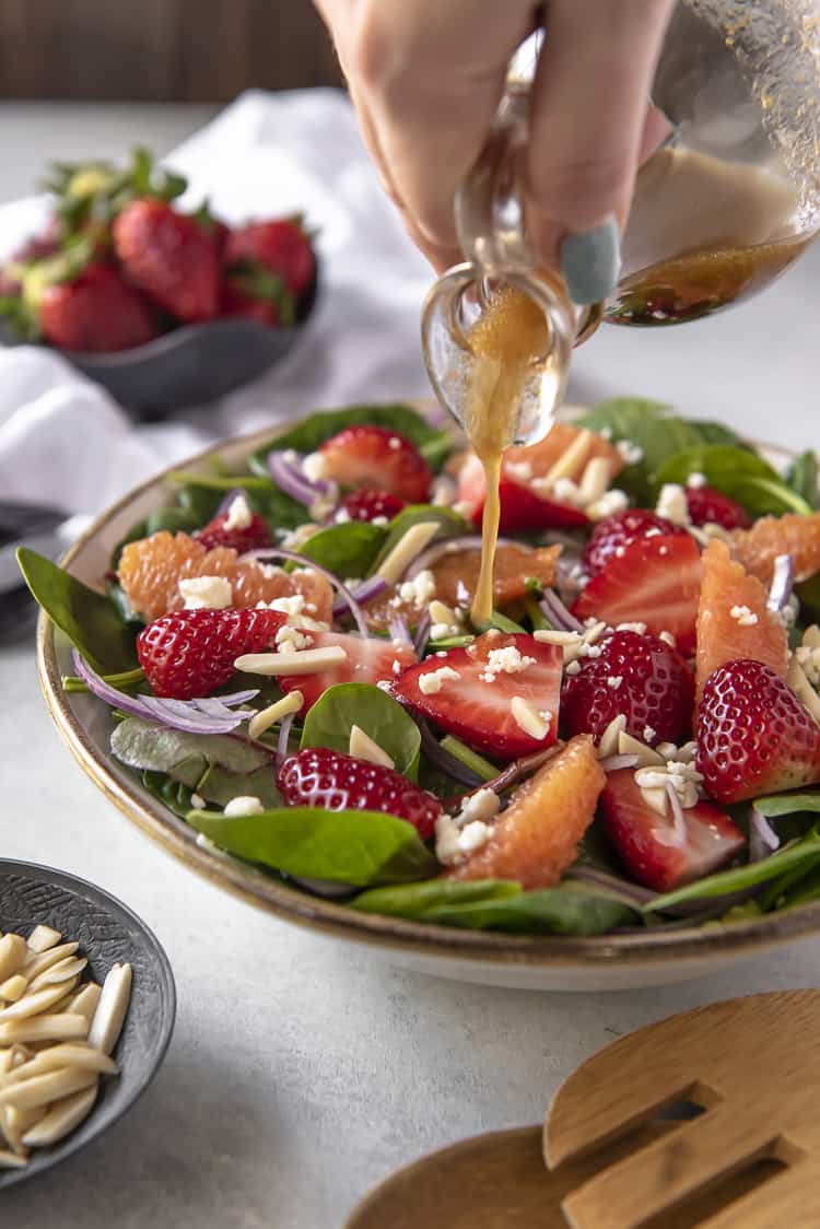 Pouring citrus vinaigrette dressing over a strawberry spinach salad with feta