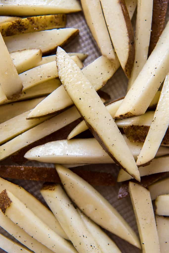 Raw, unbaked french fries tossed in oil, salt, and pepper on a pan
