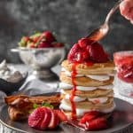 Spooning strawberry sauce on a stack of Strawberry Cheesecake Pancakes