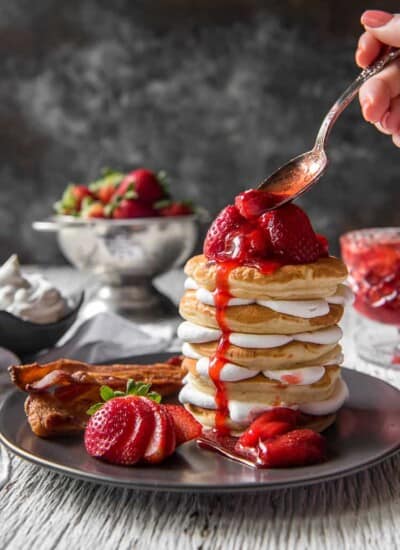 Spooning strawberry sauce on a stack of Strawberry Cheesecake Pancakes