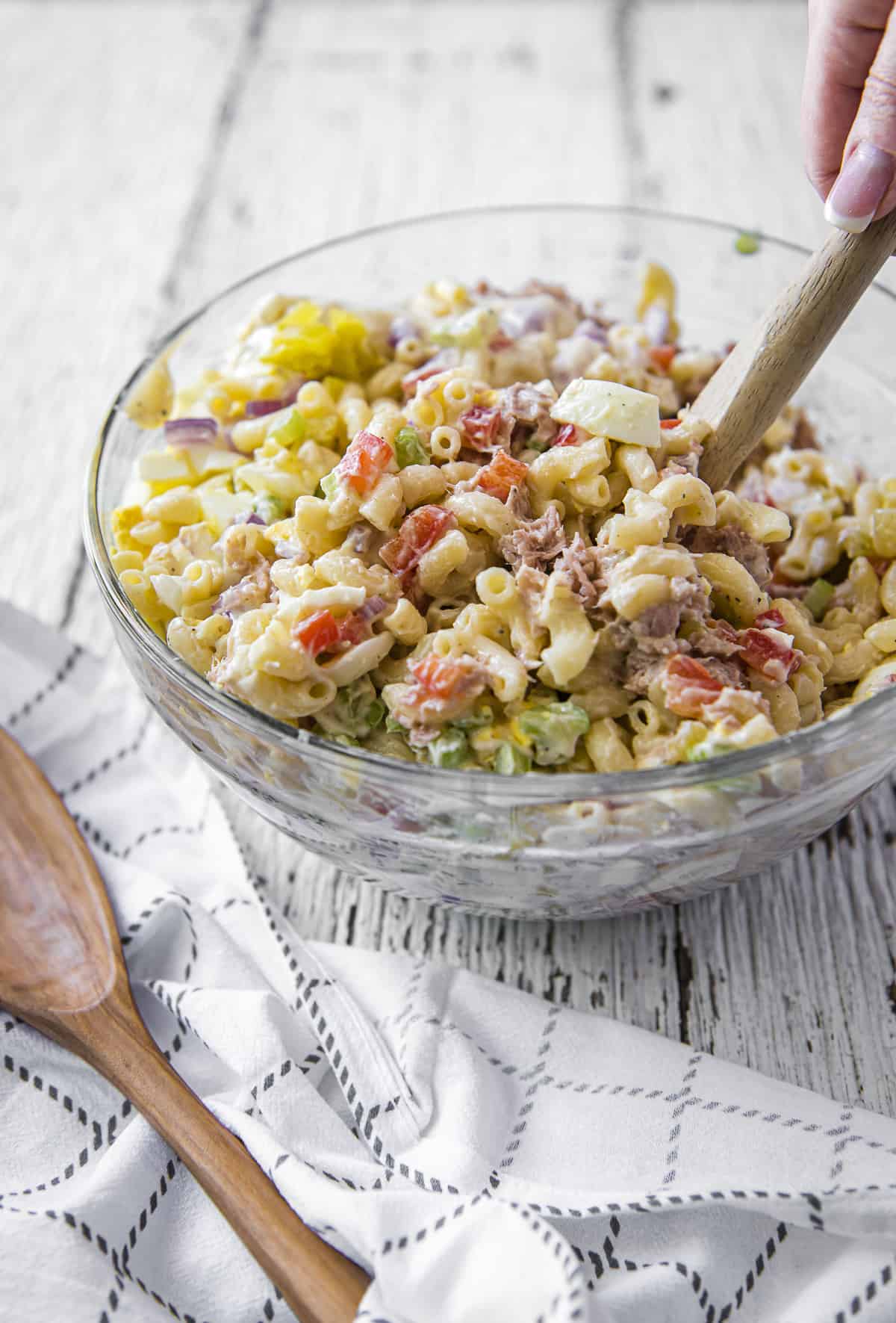 Mixing Tuna Macaroni Salad in a glass bowl with a wooden spoon