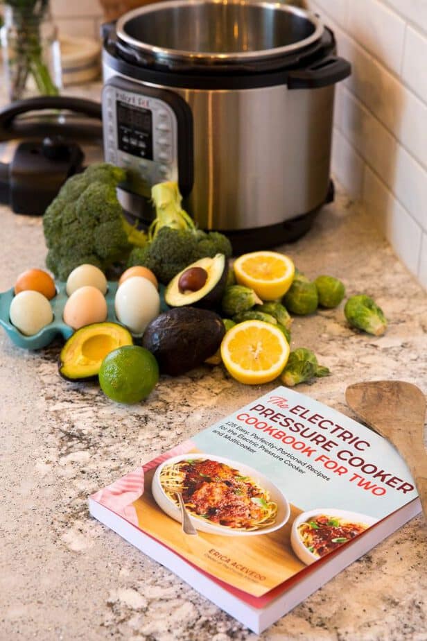 The Electric Pressure Cooker Cookbook For Two on a counter with an Instant Pot and fresh produce