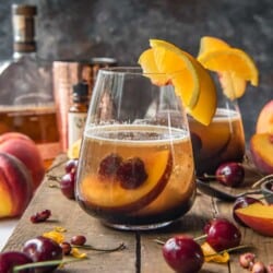 a peach old fashioned cocktail on a wood tray
