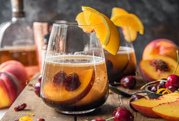 two peach old fashioned cocktails on a wood tray