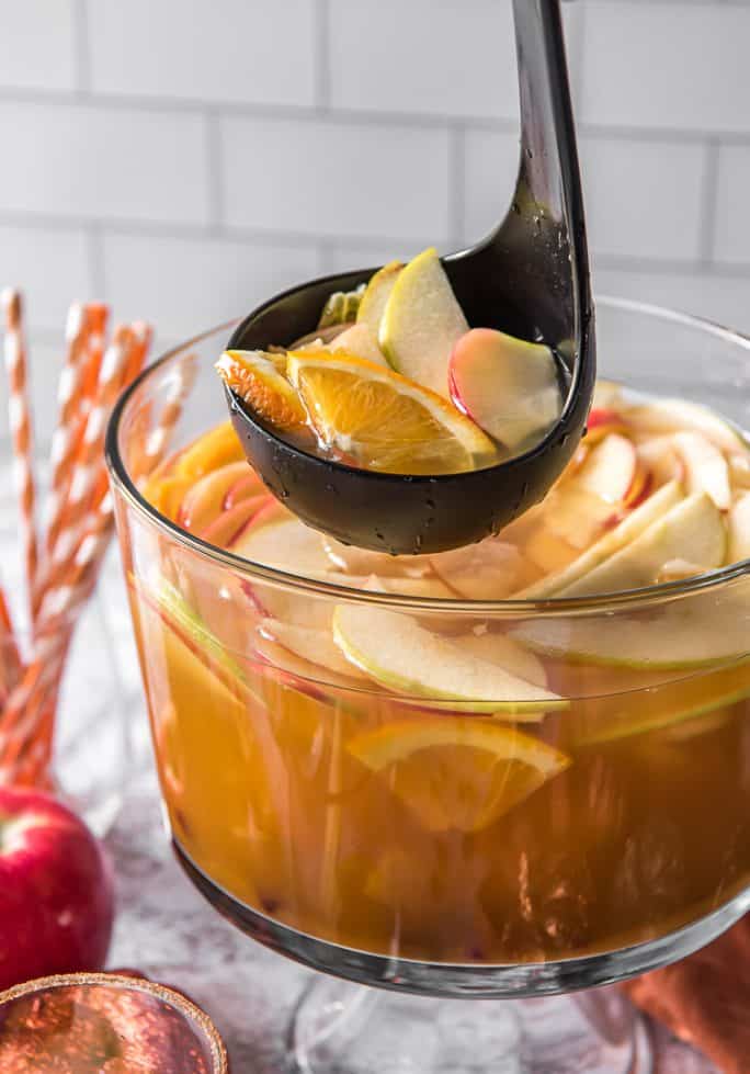a ladle scooping into a punch bowl filled with pumpkin party punch and apples