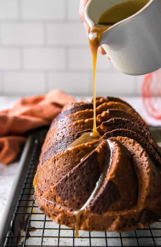 drizzling bourbon glaze on a swirled chocolate pumpkin bread loaf