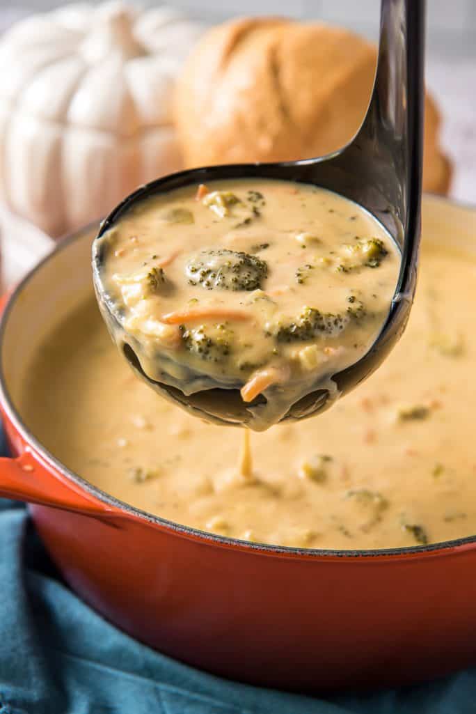a ladle full of pumpkin broccoli cheddar soup from a dutch oven