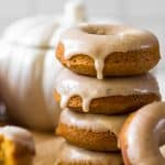 a stack of glazed pumpkin donuts with a ceramic pumpkin in the background